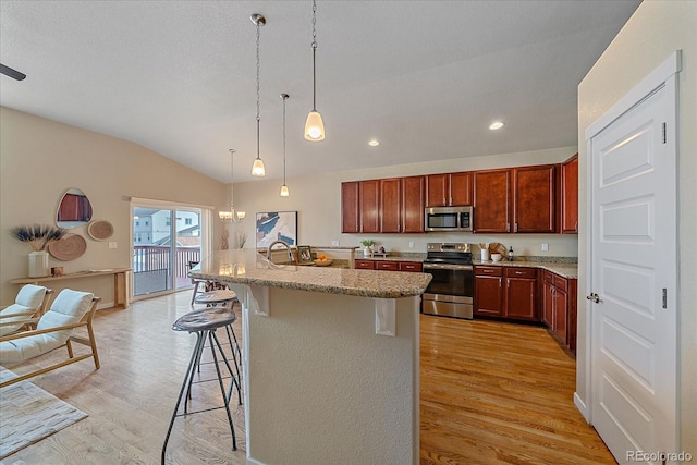 kitchen with light hardwood / wood-style flooring, stainless steel appliances, a kitchen breakfast bar, a center island with sink, and decorative light fixtures