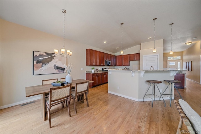 kitchen featuring lofted ceiling, light hardwood / wood-style flooring, a breakfast bar area, hanging light fixtures, and a notable chandelier