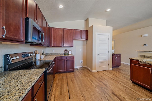 kitchen featuring light stone counters, lofted ceiling, appliances with stainless steel finishes, and light wood-type flooring