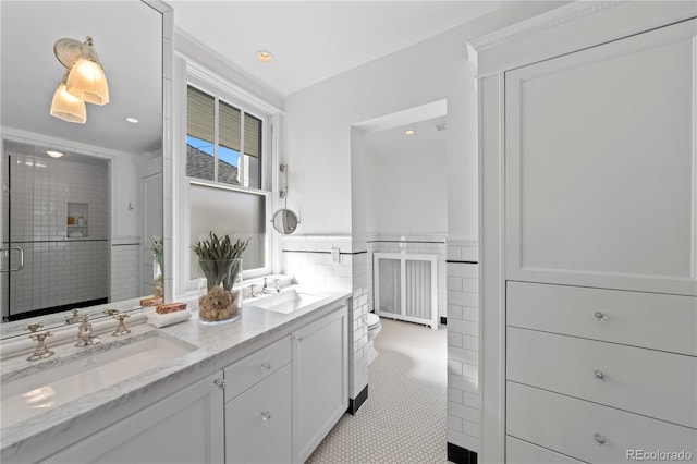 full bath featuring double vanity, tile walls, a sink, and wainscoting