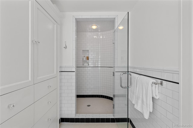 full bathroom with a wainscoted wall, a shower stall, and tile walls