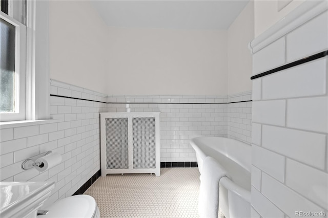bathroom with a wainscoted wall, a freestanding bath, toilet, and tile walls