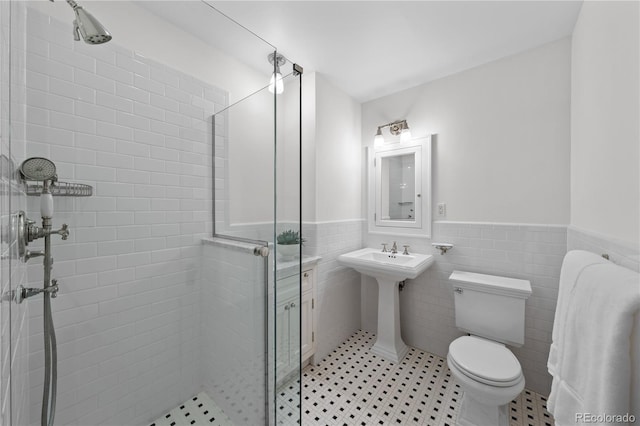 bathroom with wainscoting, a shower stall, toilet, and tile walls