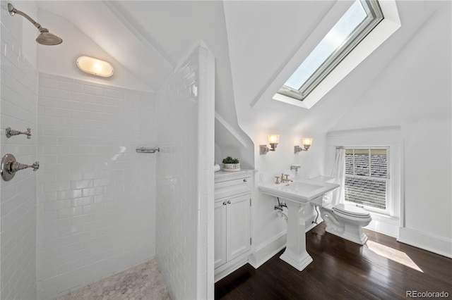 bathroom featuring toilet, vaulted ceiling with skylight, a tile shower, and wood finished floors