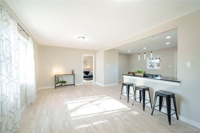 kitchen with pendant lighting, kitchen peninsula, a kitchen bar, and light hardwood / wood-style flooring