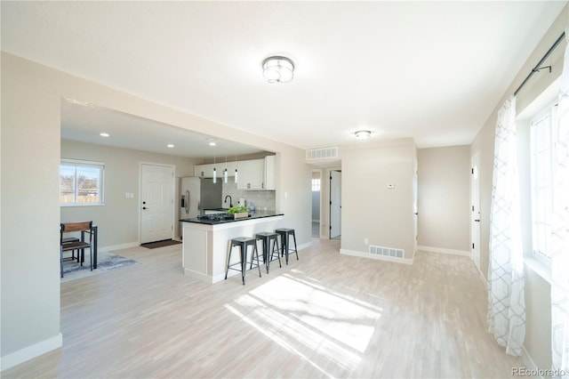 kitchen with white cabinetry, backsplash, stainless steel refrigerator with ice dispenser, a kitchen bar, and light wood-type flooring