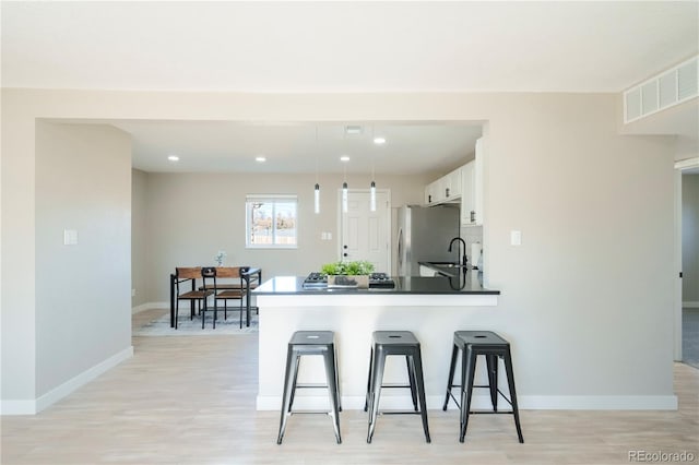 kitchen with a breakfast bar, sink, white cabinetry, stainless steel refrigerator, and kitchen peninsula