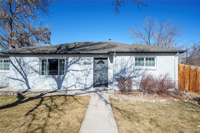 view of front of home with brick siding, fence, a front lawn, and roof with shingles