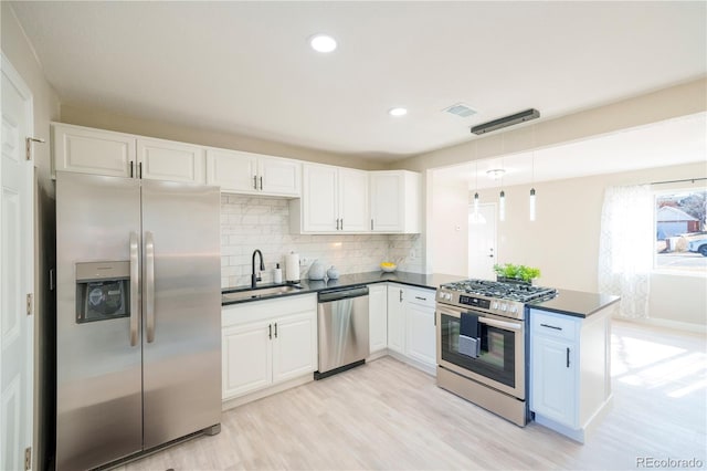 kitchen with stainless steel appliances, dark countertops, a sink, and white cabinetry