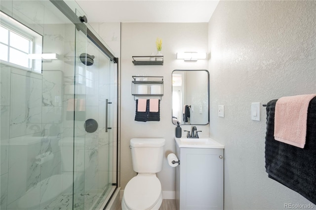 bathroom with a textured wall, toilet, vanity, and a marble finish shower