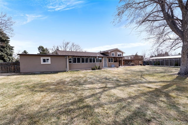 rear view of property featuring a yard, fence, a sunroom, and stucco siding