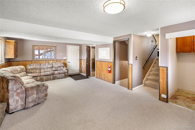 carpeted living room featuring stairway, wooden walls, wainscoting, and a textured ceiling