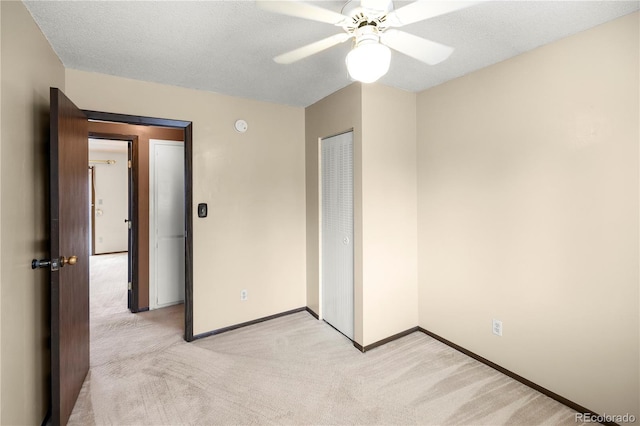 unfurnished bedroom featuring light carpet, a textured ceiling, a closet, and baseboards