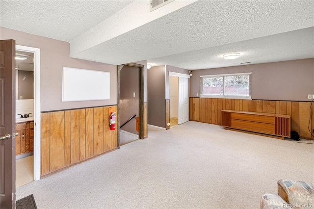 basement with a wainscoted wall, wooden walls, visible vents, and carpet flooring