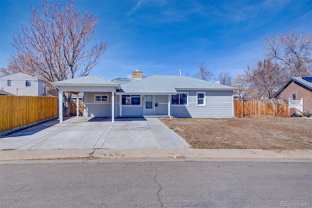 ranch-style home with roof with shingles, concrete driveway, a chimney, and fence