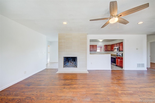 unfurnished living room featuring a tiled fireplace, wood finished floors, visible vents, and ceiling fan