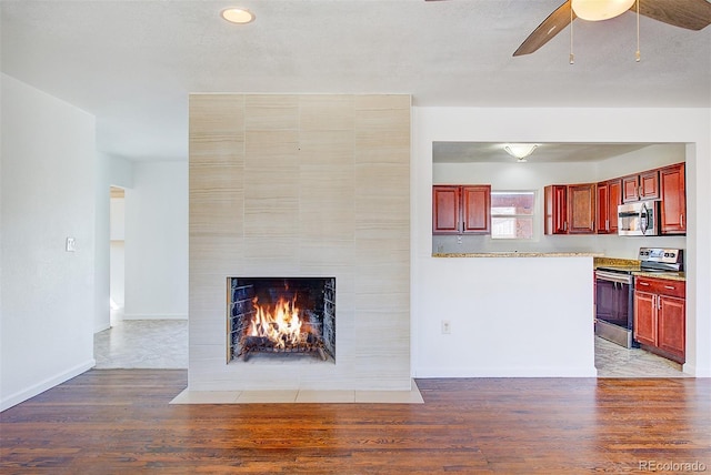 unfurnished living room with ceiling fan, a fireplace, baseboards, and light wood-style floors