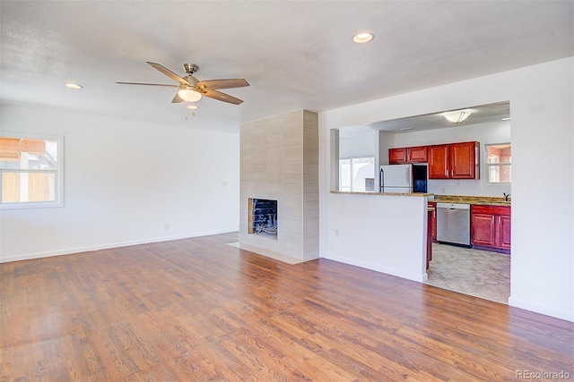 unfurnished living room with wood finished floors, a fireplace, baseboards, and a healthy amount of sunlight