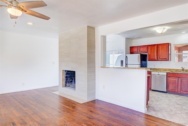 kitchen featuring dark brown cabinets, a large fireplace, light wood-style flooring, freestanding refrigerator, and stainless steel dishwasher