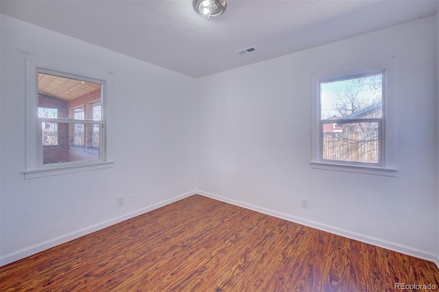 spare room featuring a wealth of natural light, visible vents, baseboards, and wood finished floors