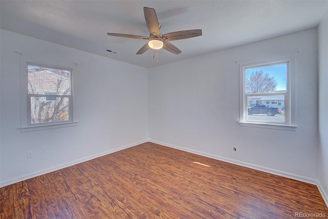 empty room featuring a wealth of natural light, baseboards, and wood finished floors