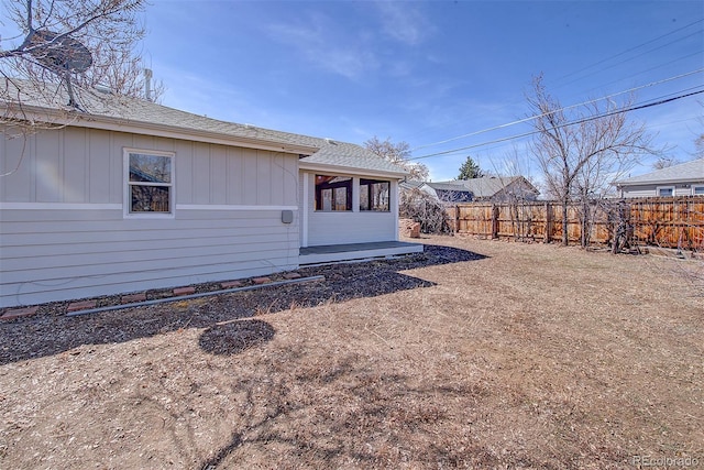 exterior space with board and batten siding, roof with shingles, and fence