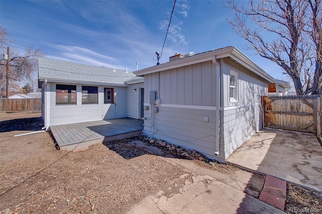 back of house with board and batten siding, a deck, and fence