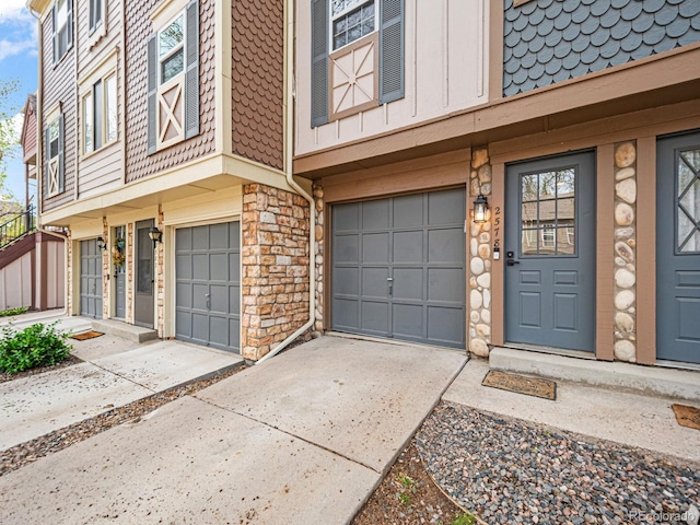entrance to property featuring concrete driveway, an attached garage, stone siding, and mansard roof