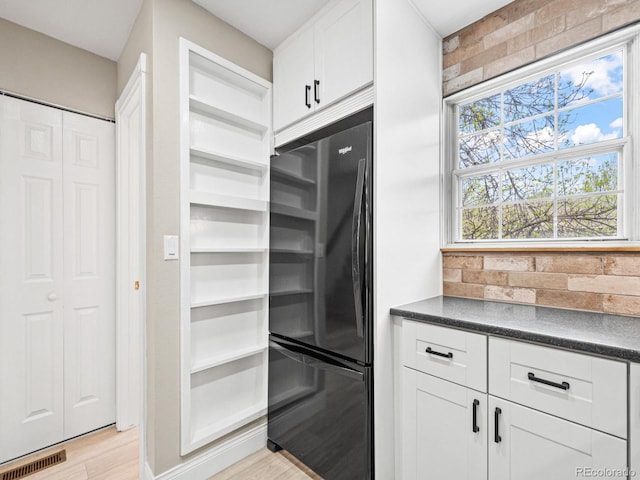 kitchen featuring freestanding refrigerator, dark countertops, white cabinets, light wood-type flooring, and tasteful backsplash