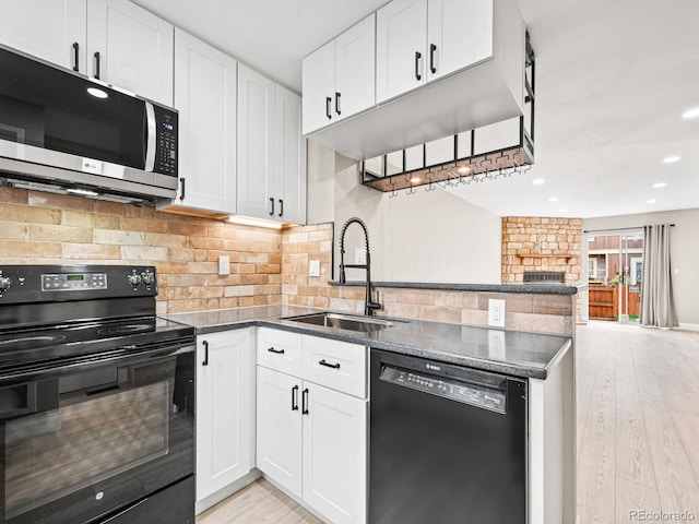 kitchen featuring black appliances, a sink, a peninsula, open floor plan, and white cabinets