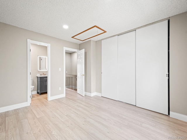 unfurnished bedroom with light wood-style floors, a closet, a textured ceiling, connected bathroom, and attic access