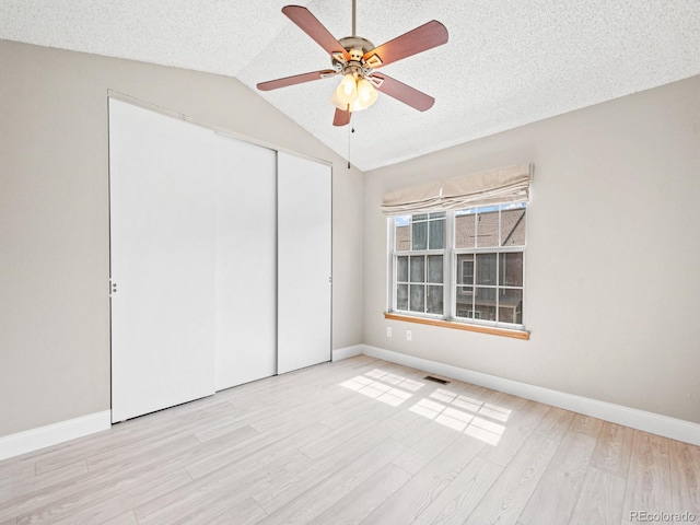 unfurnished bedroom with a closet, baseboards, vaulted ceiling, light wood-style flooring, and a ceiling fan