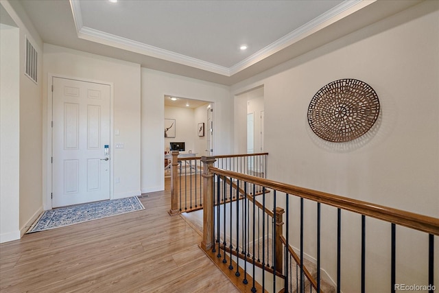 foyer entrance with baseboards, visible vents, light wood-style flooring, crown molding, and a raised ceiling