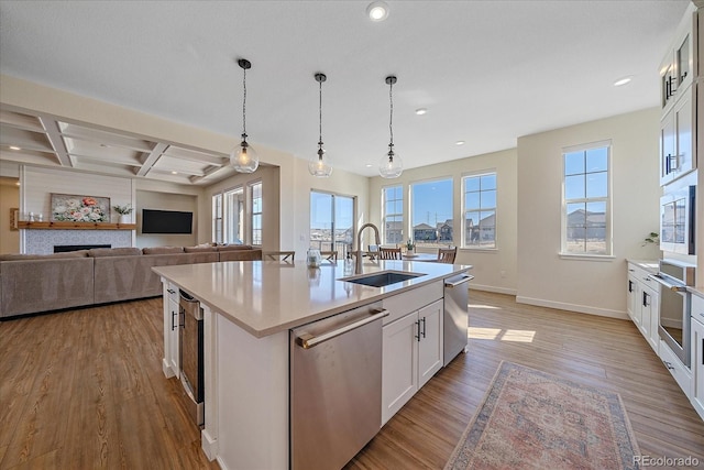 kitchen featuring an island with sink, light wood-style flooring, a sink, coffered ceiling, and stainless steel appliances