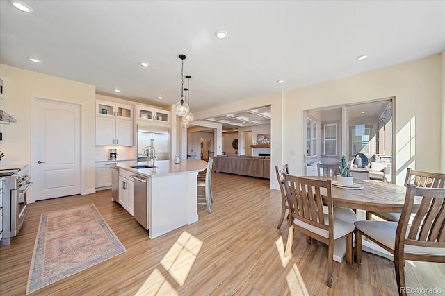 kitchen with glass insert cabinets, a center island with sink, appliances with stainless steel finishes, white cabinets, and a sink