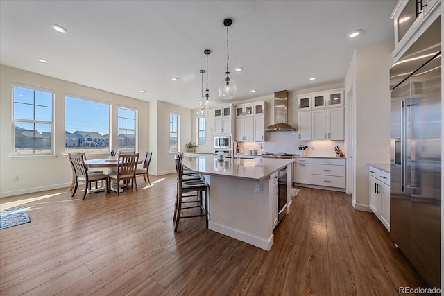 kitchen featuring dark wood-type flooring, built in appliances, decorative backsplash, wall chimney exhaust hood, and a sink