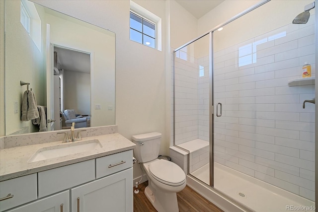 bathroom featuring wood finished floors, toilet, a stall shower, and vanity