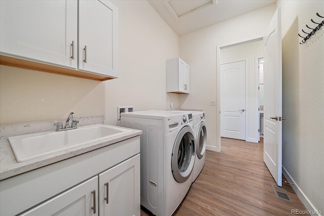 laundry area with baseboards, light wood-style flooring, cabinet space, a sink, and washing machine and dryer