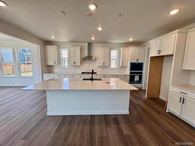 245 Wooten Ave, Brighton, CO 80601 - kitchen with wall chimney range hood, white cabinets, decorative backsplash, a center island with sink, and recessed lighting