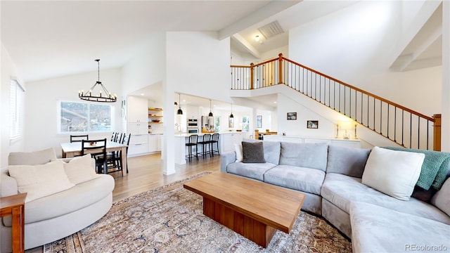 living room with light hardwood / wood-style floors, beam ceiling, high vaulted ceiling, and an inviting chandelier