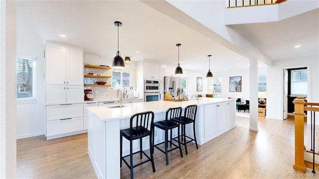 kitchen with white cabinets, a spacious island, hanging light fixtures, appliances with stainless steel finishes, and light hardwood / wood-style floors