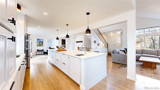 kitchen featuring sink, light hardwood / wood-style flooring, an island with sink, decorative light fixtures, and white cabinets