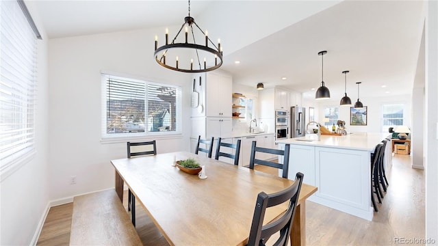 dining space featuring a notable chandelier, light hardwood / wood-style floors, sink, and vaulted ceiling