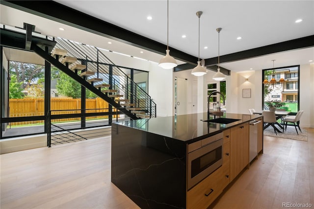 kitchen with pendant lighting, an island with sink, sink, stainless steel appliances, and light wood-type flooring