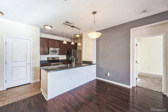 kitchen with dark stone counters, appliances with stainless steel finishes, decorative light fixtures, dark hardwood / wood-style flooring, and dark brown cabinetry