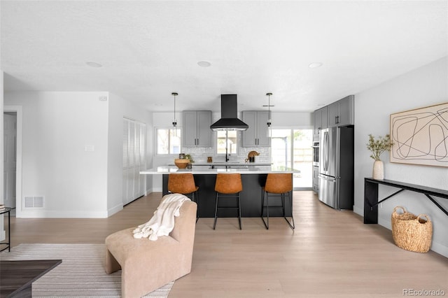 3065 S Eudora St, Denver, CO 80222 - kitchen featuring appliances with stainless steel finishes, wall chimney range hood, light countertops, light wood-style flooring, and a breakfast bar area