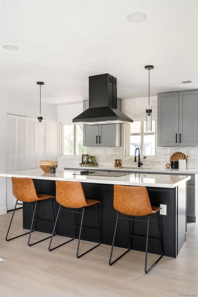 3065 S Eudora St, Denver, CO 80222 - kitchen featuring island exhaust hood, decorative backsplash, light wood finished floors, light countertops, and a kitchen bar