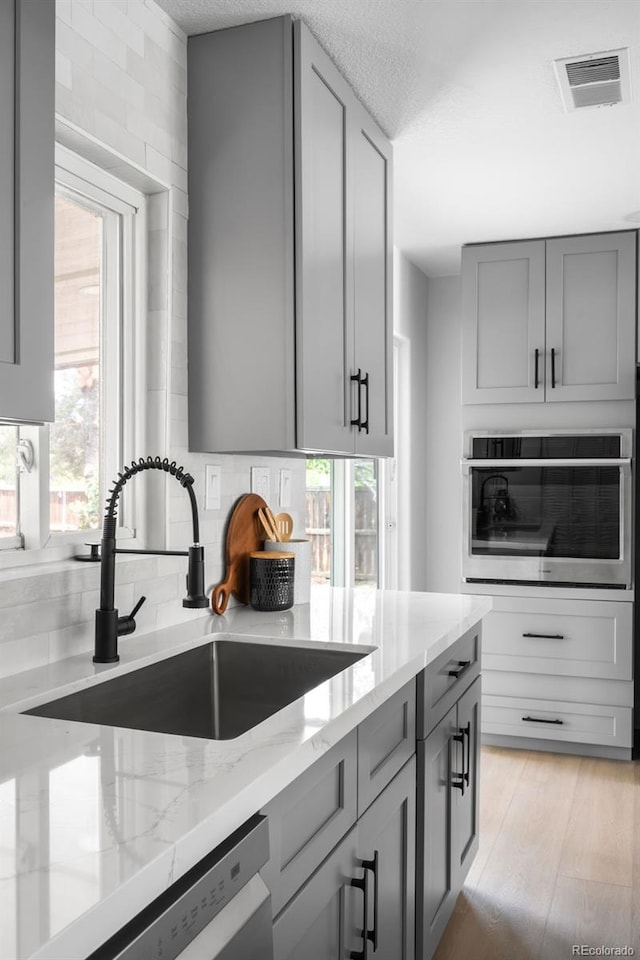 3065 S Eudora St, Denver, CO 80222 - kitchen with stainless steel appliances, gray cabinets, a sink, light stone countertops, and a textured ceiling