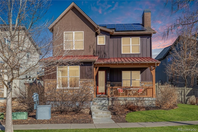 traditional home with a chimney, solar panels, a porch, board and batten siding, and stone siding