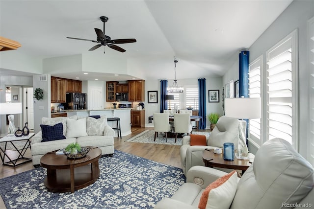 living area featuring ceiling fan with notable chandelier, vaulted ceiling, light wood-style flooring, and recessed lighting